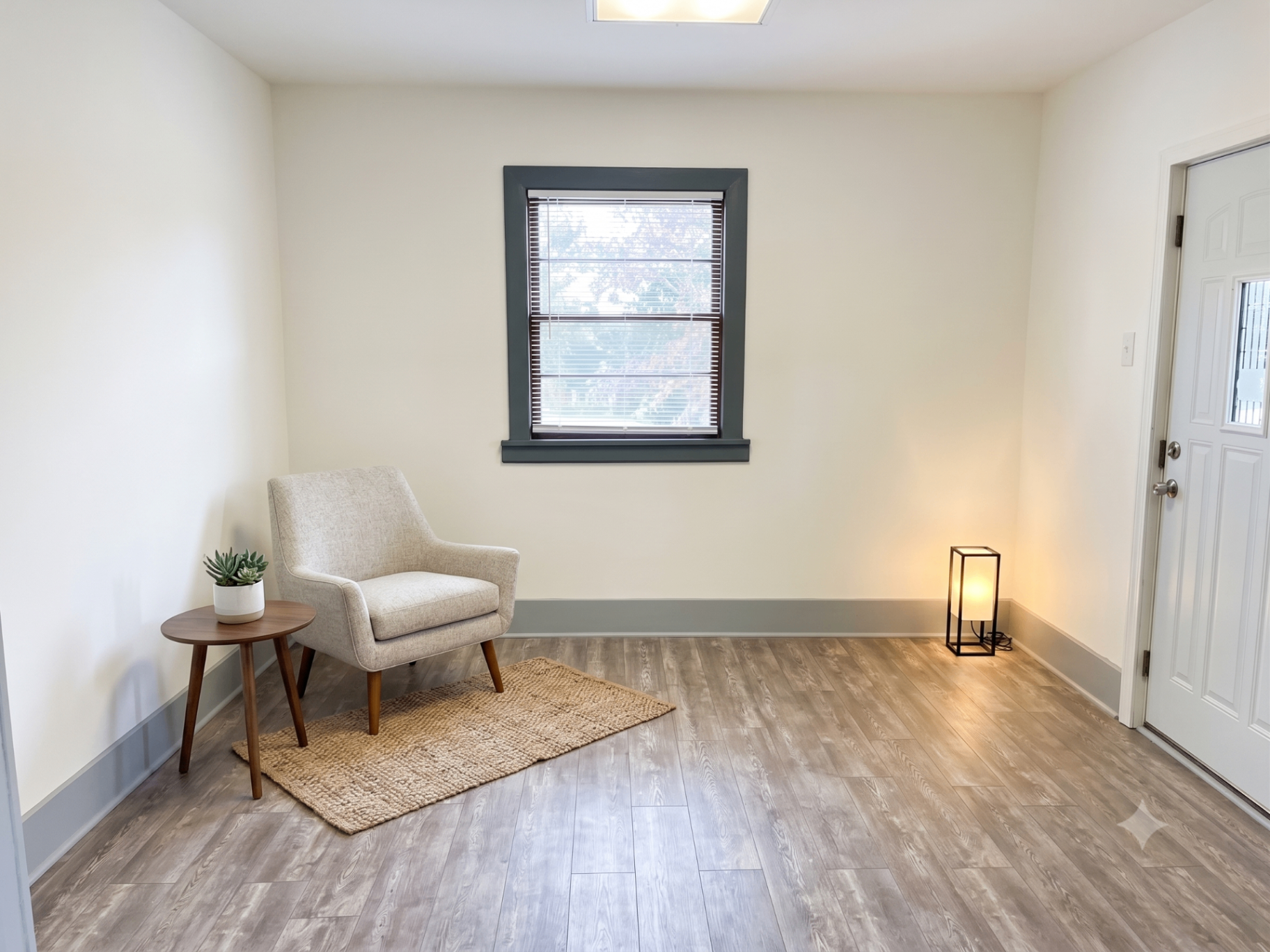 Same living room cleaned, painted and staged with a modern chair and rug, move-in ready for the next tenant