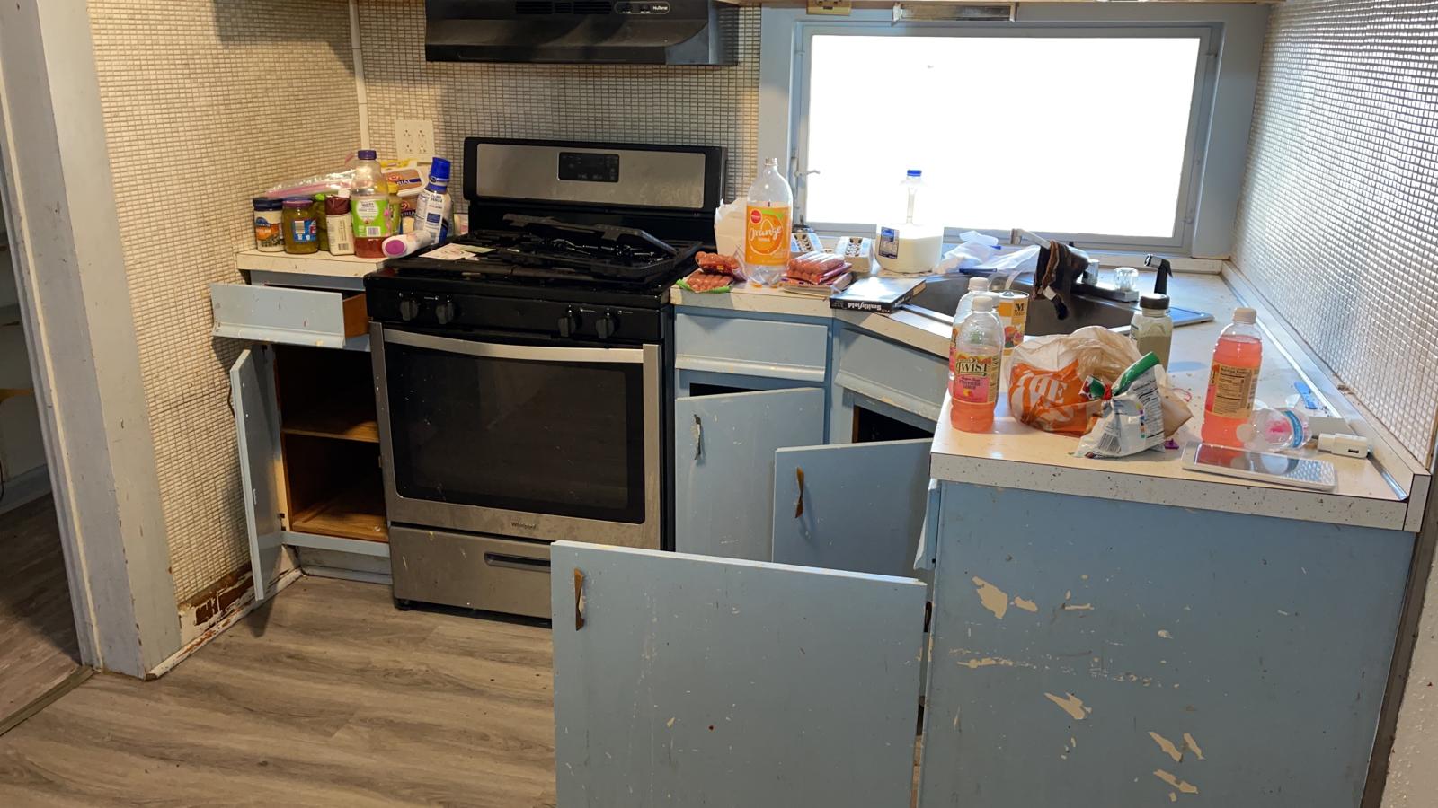 Dirty rental kitchen with damaged blue cabinets, trash and leftover food on countertops after tenant moved out in St. Louis